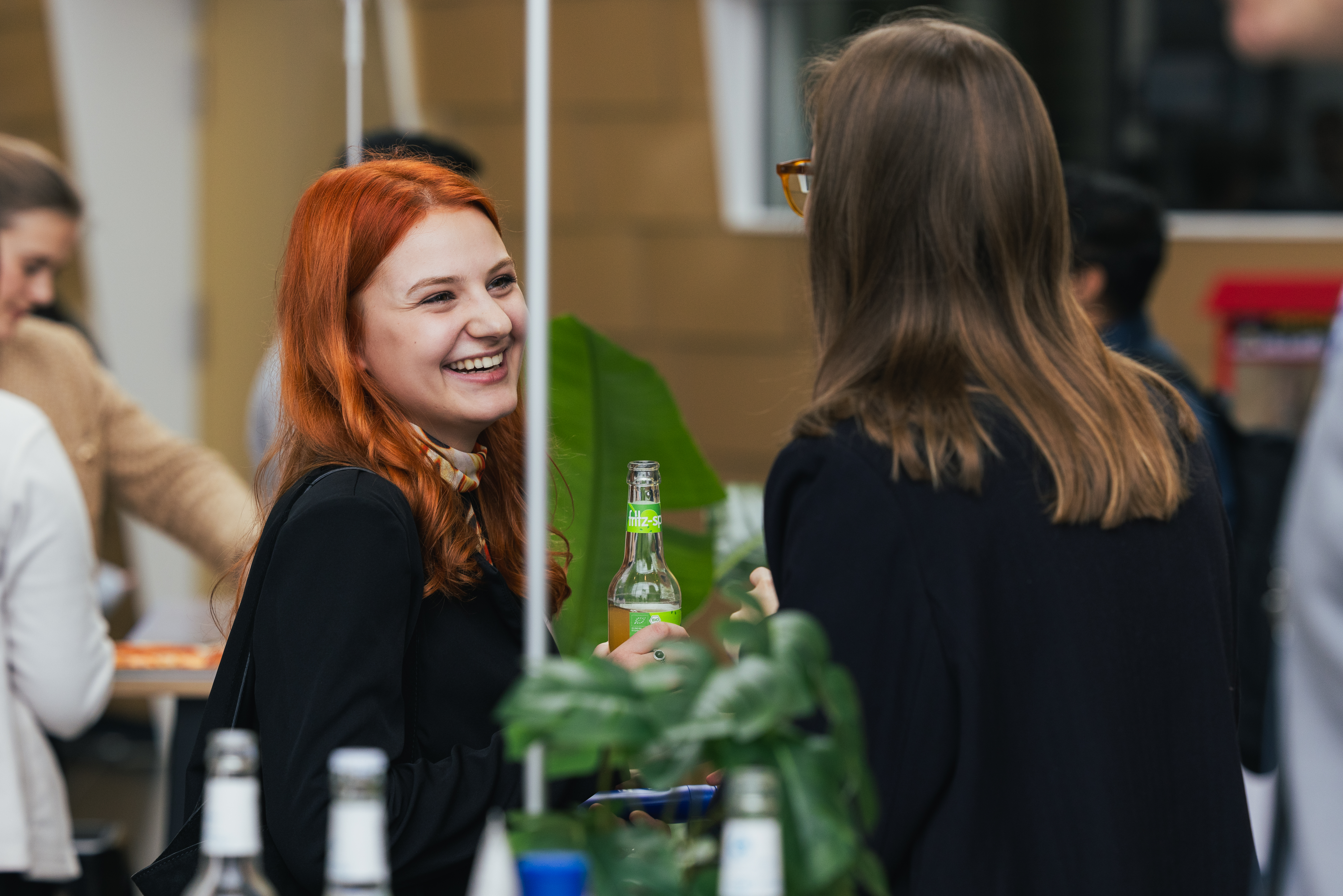 Two women at the table, smiling and chatting while holding drinks